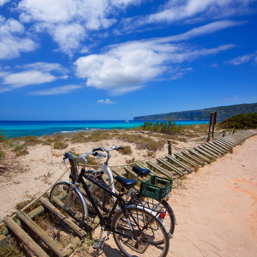 Des voyageurs chargent leurs vélos sur un ferry amarré dans un port grec entouré de villages blancs.